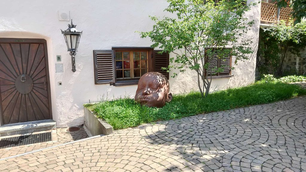 eine Kopffigur aus Stahlblech vor einem alten Haus